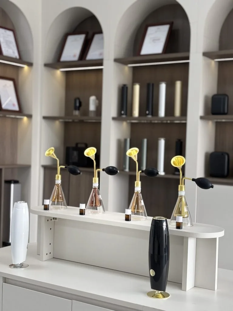 Fragrance display bottles and diffuser models in front of showroom shelves.